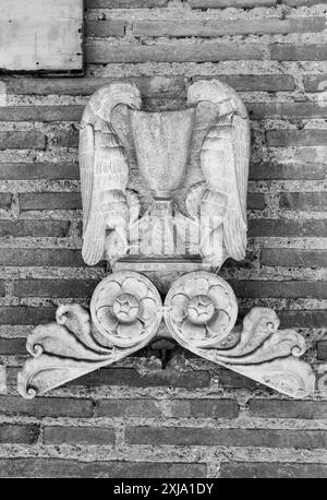 Black and white photo of sculpture in stone hanging on a bricks wall representing two eagles drinking from a chalice Stock Photo