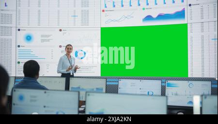 Caucasian Female Data Scientist Giving Presentation On Big Digital Screen With Green Screen Chromakey In Monitoring Office. Team Of Deep Learning Company Employees Listening Behind Desktop Computers. Stock Photo