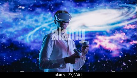 Young Male Wearing a Virtual Reality Headset and Using Controllers in a Futuristic Room with Digital Space Animation. Scientist Exploring VR Universe, Different Galaxies, Planets, Space and Time Stock Photo