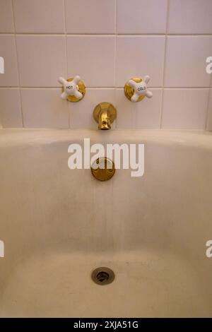 Close-up of old-fashioned bathtub faucet and drain in a tiled white bathroom Stock Photo