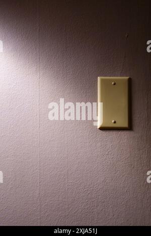A plate on the wall covering an electrical plug plate in shadow. Stock Photo