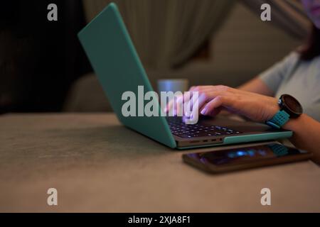 Close-up of hands typing on a laptop in a cozy home setting, with a coffee mug in the background. Concept of remote work and productivity. Stock Photo
