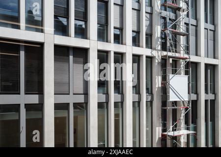 A contemporary office building facade with large windows and vertical columns. The image features scaffolding set up on the side. Stock Photo