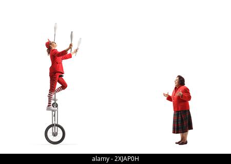 Amused elderly woman watching an acrobat riding a giraffe unicycle and juggling isolated on white background Stock Photo