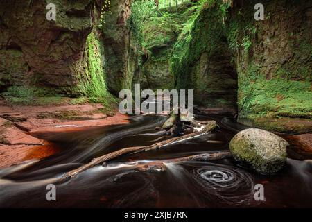 Long exposure image of Devil's Pulpit gorge in Finnich Glen, Scotland, with dark red river flowing through green moss covered deep ravine Stock Photo