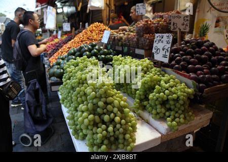 Two men wearing summer clothes buy fruit at a Machane Yehuda Market stand where grapes, plums, avocados and cherries are sold Stock Photo