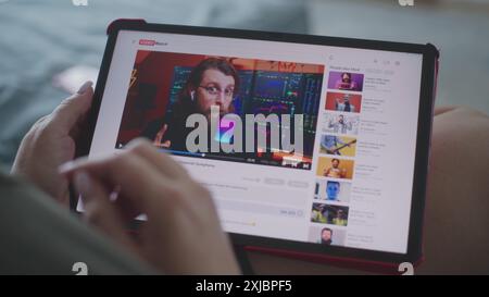 Caucasian woman watches educational video of blogger about stock trading using tablet computer while lying on sofa. Tablet screen shows video hosting website interface with video content. Close Up. Stock Photo