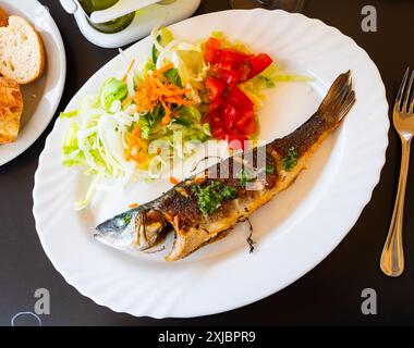 There is plate with fried whole carcass zander fish and mix vegetable salad on table Stock Photo