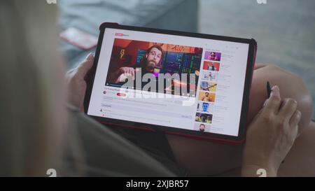 Caucasian woman watches educational video of blogger about stock trading using tablet computer while lying on sofa. Tablet screen shows video hosting website interface with video content. Close Up. Stock Photo