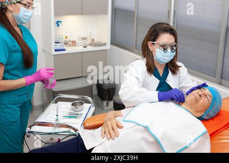 Dermatologist carrying out a skin biopsy on the face of a senior adult ...