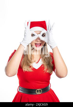 young blonde woman dressed as mama claus expressive looking at camera making a gesture with her hands as if she had glasses isolated on white backgrou Stock Photo