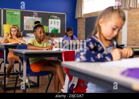 Multiracial schoolgirls studying while sitting at desk in classroom Stock Photo