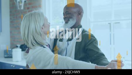 Image of multiple up arrow over diverse couple dancing wearing apron at home Stock Photo