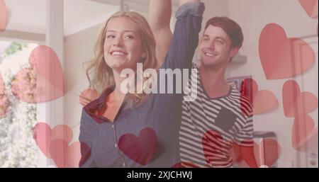 Image of hearts over happy diverse couple dancing at home. Love, relationship, home and lifestyle concept digitally generated image. Stock Photo