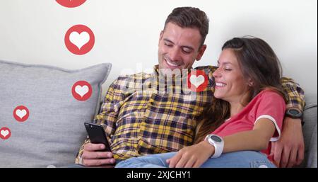 Image of hearts over happy diverse couple using smartphone at home Stock Photo