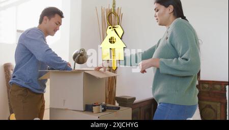 Image of golden key and house over diverse couple carrying cartons at home. Moving house and home concept digitally generated image. Stock Photo