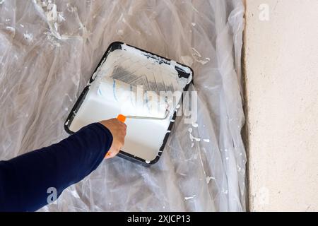 Close-up of hands using paint roller and white paint on the paint tray. Home improvement and house painting concept. Stock Photo