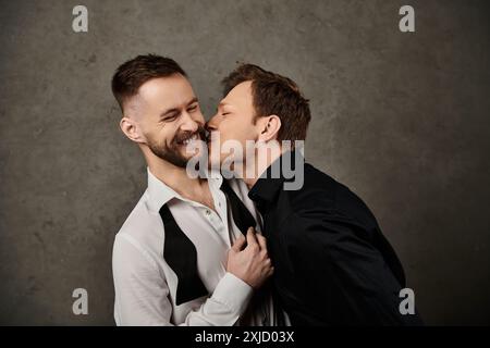 Two men in suits kiss, laughter against grey background. Stock Photo