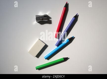 Photo of office equipment. Scattered randomly on a white background. Colored pencils, eraser, pencil sharpeners. Back to school. Pencils made of black Stock Photo