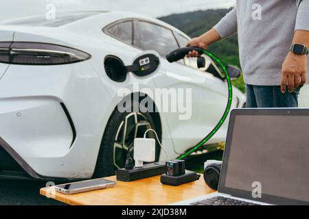 Businessman online working and relaxing outdoor activity using V2L technology where an electric vehicle acts as a mobile battery Stock Photo
