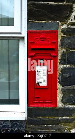Royal Mail post box set in stone next to window, the box is red with GR emblem and info plate in white Stock Photo