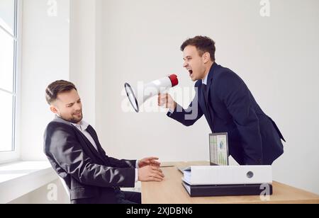 Angry boss with megaphone shouts at man in office, close-up Stock Photo