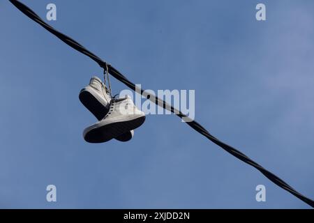 Sneakers hanging on a wire against blue sky. Stock Photo