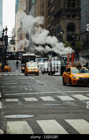 Yellow cabs and busses moving past steam vents on Madison Avenue, white lines of multiple Zebra Crossings, a classic New York City street scene. Stock Photo