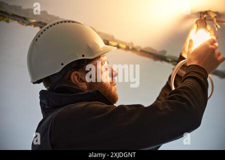 Portrait of male electrician, wearing hard hat,  installing temporary light bulb on the ceiling. Stock Photo