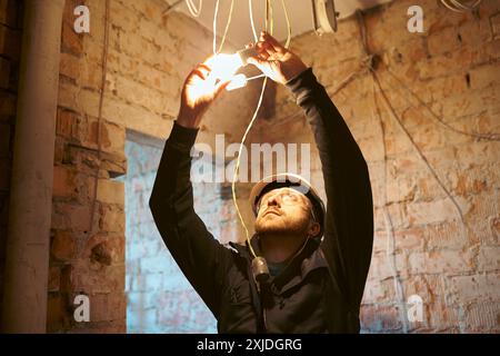 Male construction worker installing temporary light bulb on site. Stock Photo