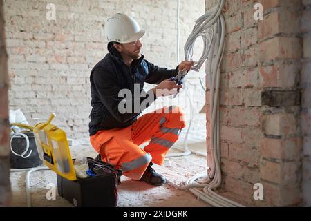Electrical contractor working with cables on construction site during installation process. Stock Photo