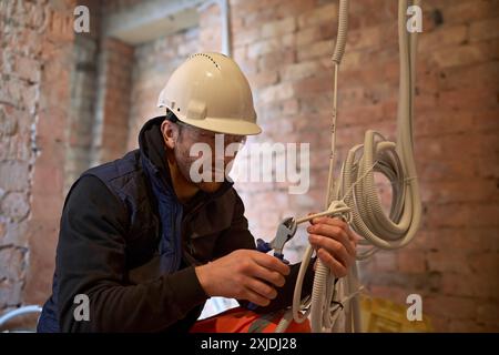 Close up of electrician working with multiple cables and holding wire cutters. Electrician in the process of cutting white cable with wire cutters. Stock Photo