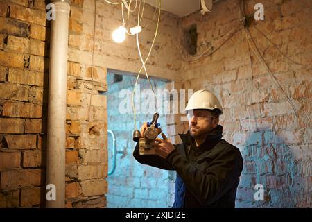 Electrical contractor working with cables on construction site during installation process. Stock Photo