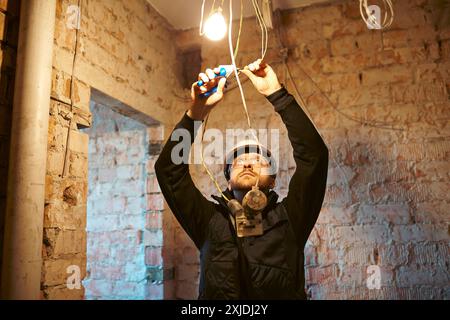 Male construction worker installing temporary light bulb on building under renovation. Stock Photo