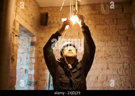 Male construction worker installing temporary light bulb on building under renovation. Stock Photo