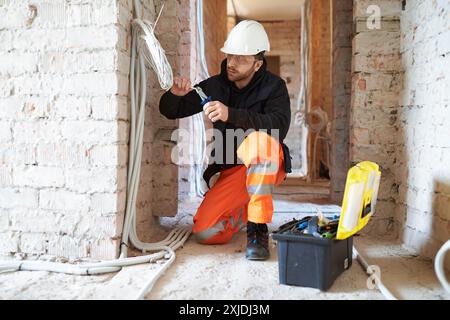 Electrical contractor working with cables on construction site during installation process. Stock Photo