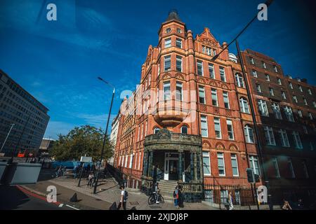 London, UK - October 09, 2023 : A red brick building with ornate details stands on a street corner in London, UK. Pedestrians walk past while a bus dr Stock Photo