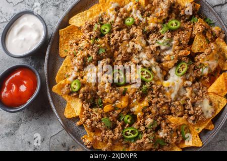 Traditional nachos with ground beef, cheddar cheese and jalapeno  pepper served with sauces closeup on the plate on the table. Horizontal top view fro Stock Photo