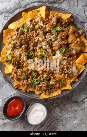 Cheesy Beef Nachos Tortilla chips covered with seasoned ground beef and melted cheese closeup on the plate on the table. Vertical top view from above Stock Photo