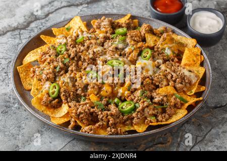 Traditional nachos with ground beef, cheddar cheese and jalapeno  pepper served with sauces closeup on the plate on the table. Horizontal Stock Photo
