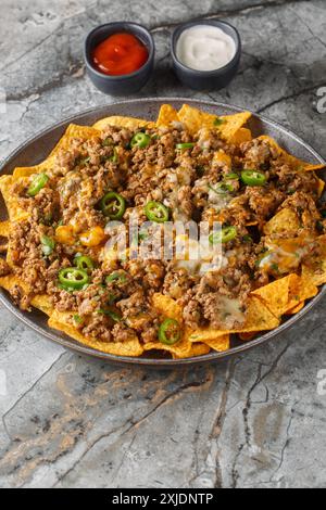 Loaded Beef and Cheese Nachos with jalapeno peppers and sauces closeup on the plate on the table. Vertical Stock Photo