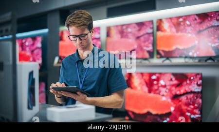 Young Productive Salesperson in Home Electronics Store Working on Tablet Computer. Professional Staff Member Using Software to Monitor Inventory, Track Device Sales, and Provide Customer Service Stock Photo