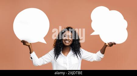 Smiling Woman Holding Blank Speech Bubbles Against a Peach Background Stock Photo