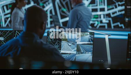 African Specialist in a Dark High-Tech Monitoring Room, Concentrated on Live CCTV Footage with Traffic Situation. Black Technical Support Manager Using Computer for Solving an Issue for a Client Stock Photo