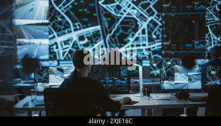 Establishing Shot: Dark Room with Multiethnic Specialists Working on Desktop Computers. Big LED Screen Shows Surveillance Satellite Data, City Map, and CCTV Traffic Footage Reports Stock Photo