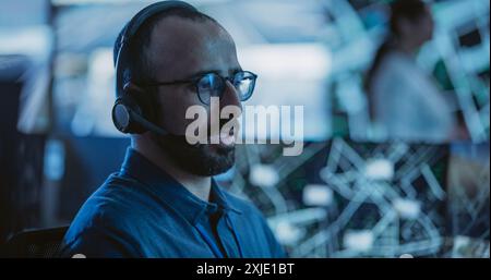 Portrait of a Surveillance Officer Wearing a Headset, Working in a Central Office Hub for Cybersecurity Operations, Control and Monitoring for Managing National Security and Technology Stock Photo
