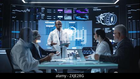 International Aerospace Research and Manufacturing Company Working on Turbine Jet Engine. Engineer Having a Meeting with a Group of Multiethnic Scientists in a Room with Big Digital Screen Stock Photo