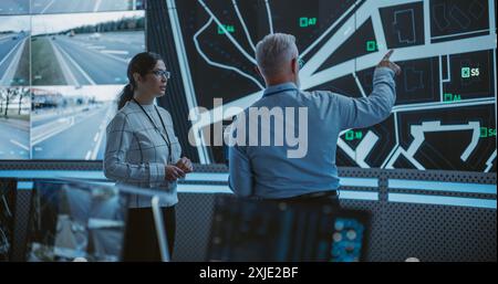 Male and Female Having a Discussion in Front of a Screen with Surveillance CCTV Footage. Team of Software Developers, Engineers and Data Scientists Working in a Modern Logistics Technology Company Stock Photo