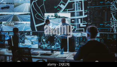 Futuristic City Logistics Planning Monitoring Center with Diverse Male and Female Officers Analyzing Live CCTV Footage on a Big Digital Screen. Talented Team of Specialists Working in Office Stock Photo