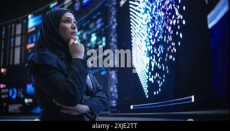 Portrait of a Smart Focused Middle Eastern Software Engineer Analyzing Neural Network Big Data on a Digital Screen. Young Arab Woman in Hijab Working in an Innovative Internet Service Company Stock Photo